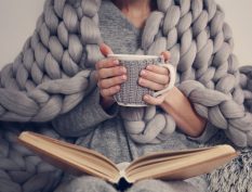 Woman with a blanket, book, and coffee mug