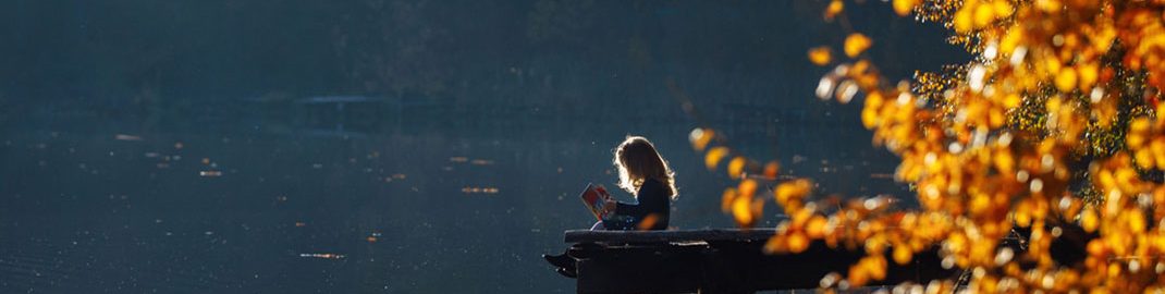 Girl reading by a lake during autumn